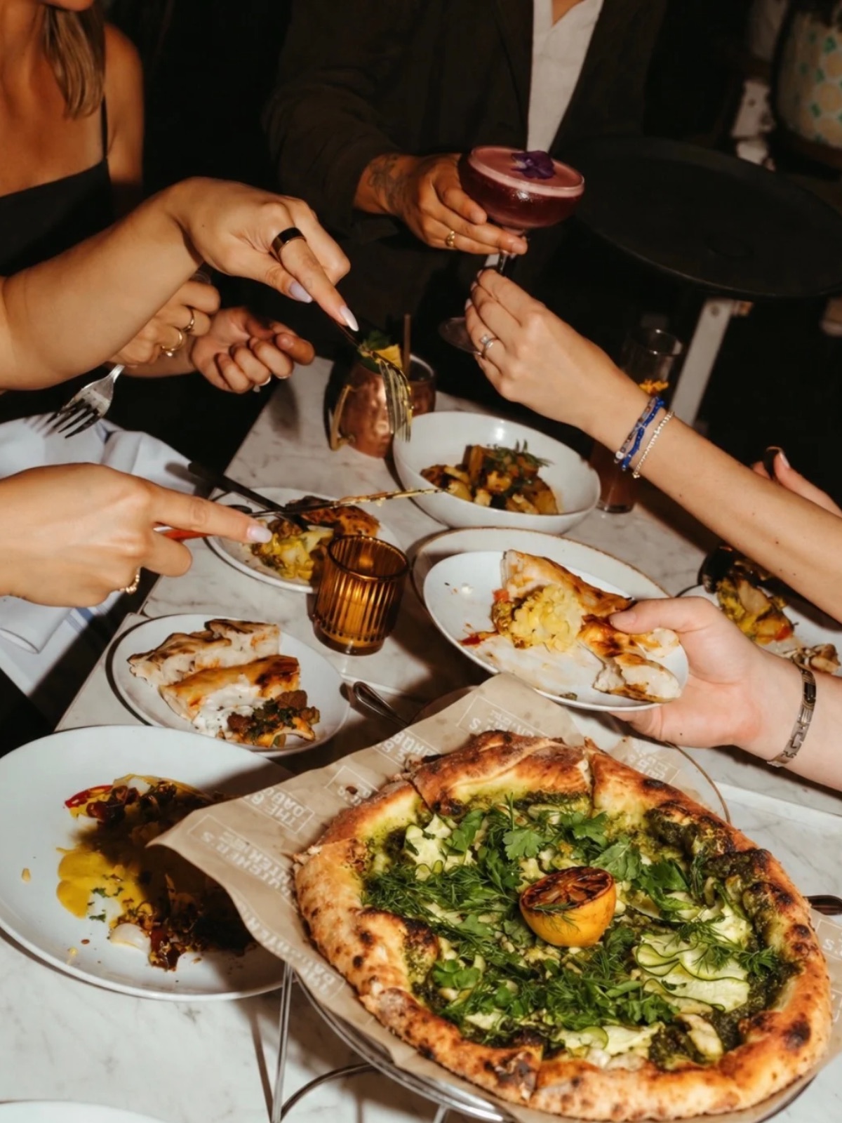 An image of people eating pizza with drinks at The Butcher's Daughter.